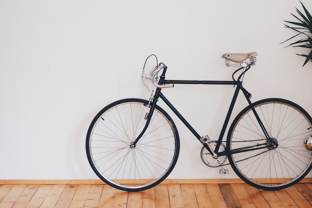 Black bike against a white wall and a wooden floor